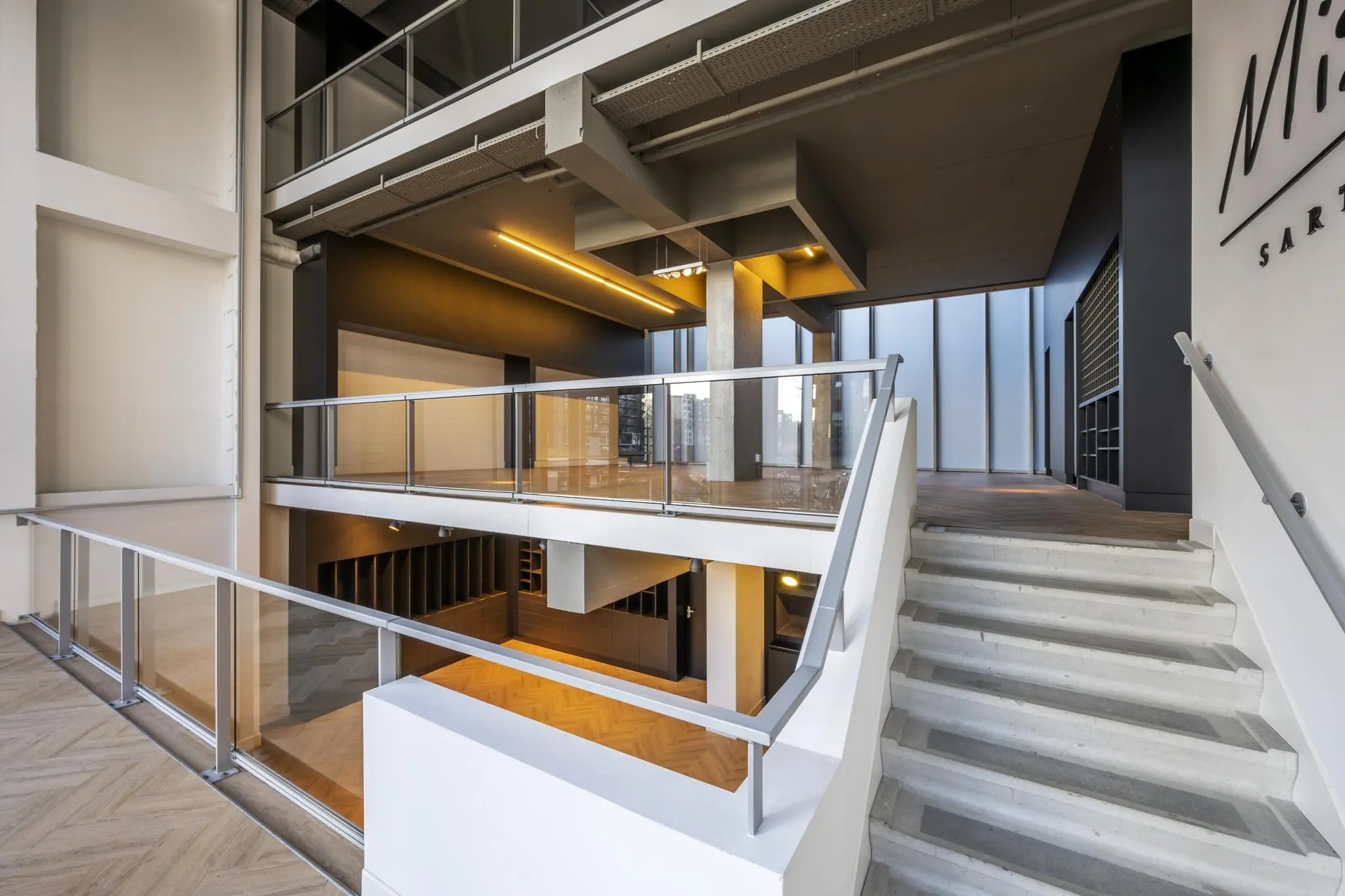 Moderne, open entreehal met glazen balustrades en betonnen trap aan het George Gershwinplein.